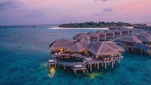 Bungalows over vandet med stråtækte tage, forbundet af gangbroer, og fri udsigt til havet.