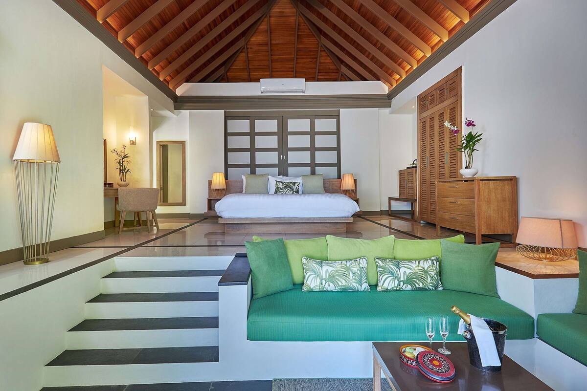 Ein geräumiges Zimmer mit einem großen Bett, einem grünen Sofa, einem Holzkasten und einer Treppe, die eine weitere Ebene hinaufführt.