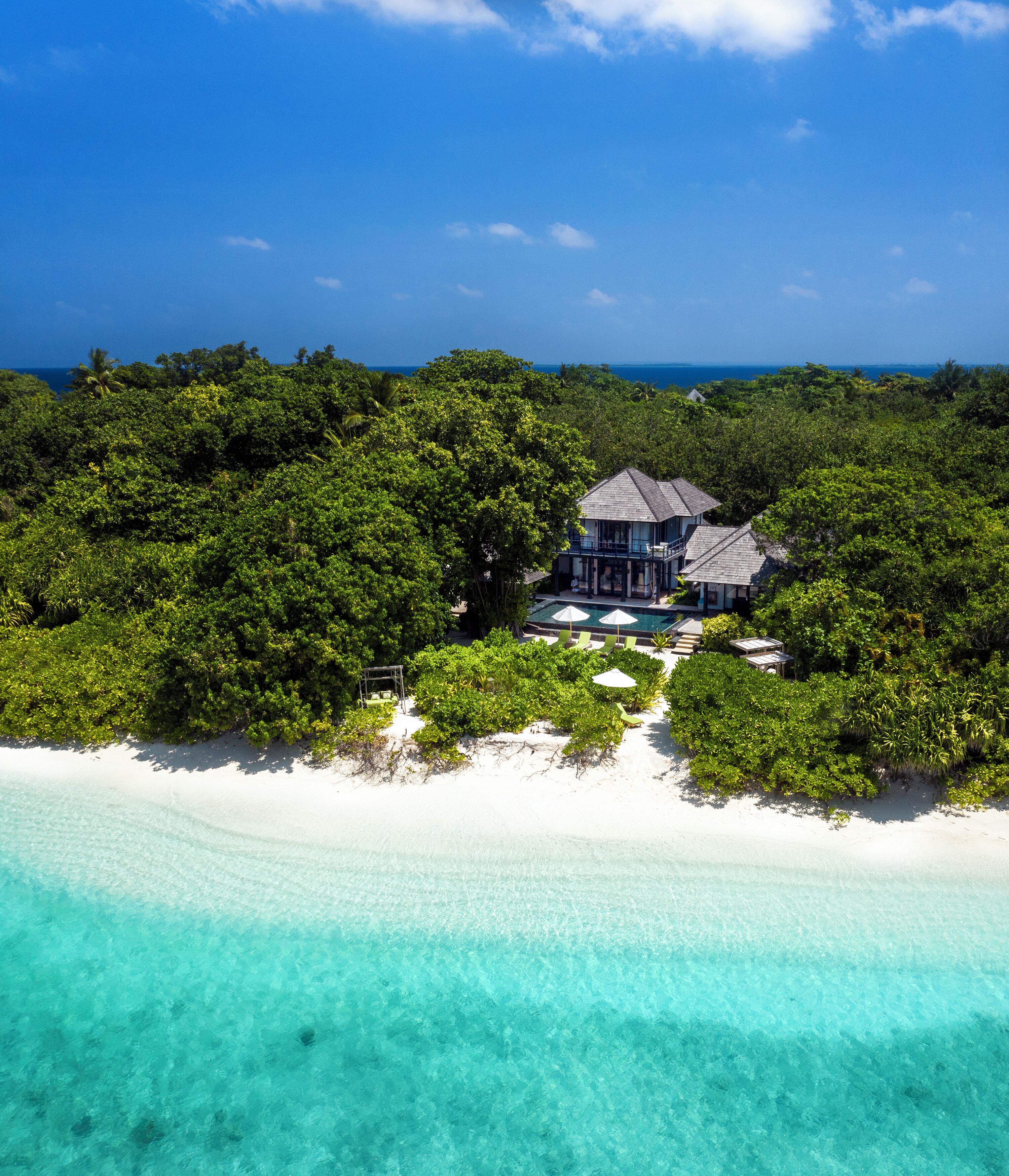 A beachfront property with a pool, surrounded by lush greenery and a clear blue ocean.