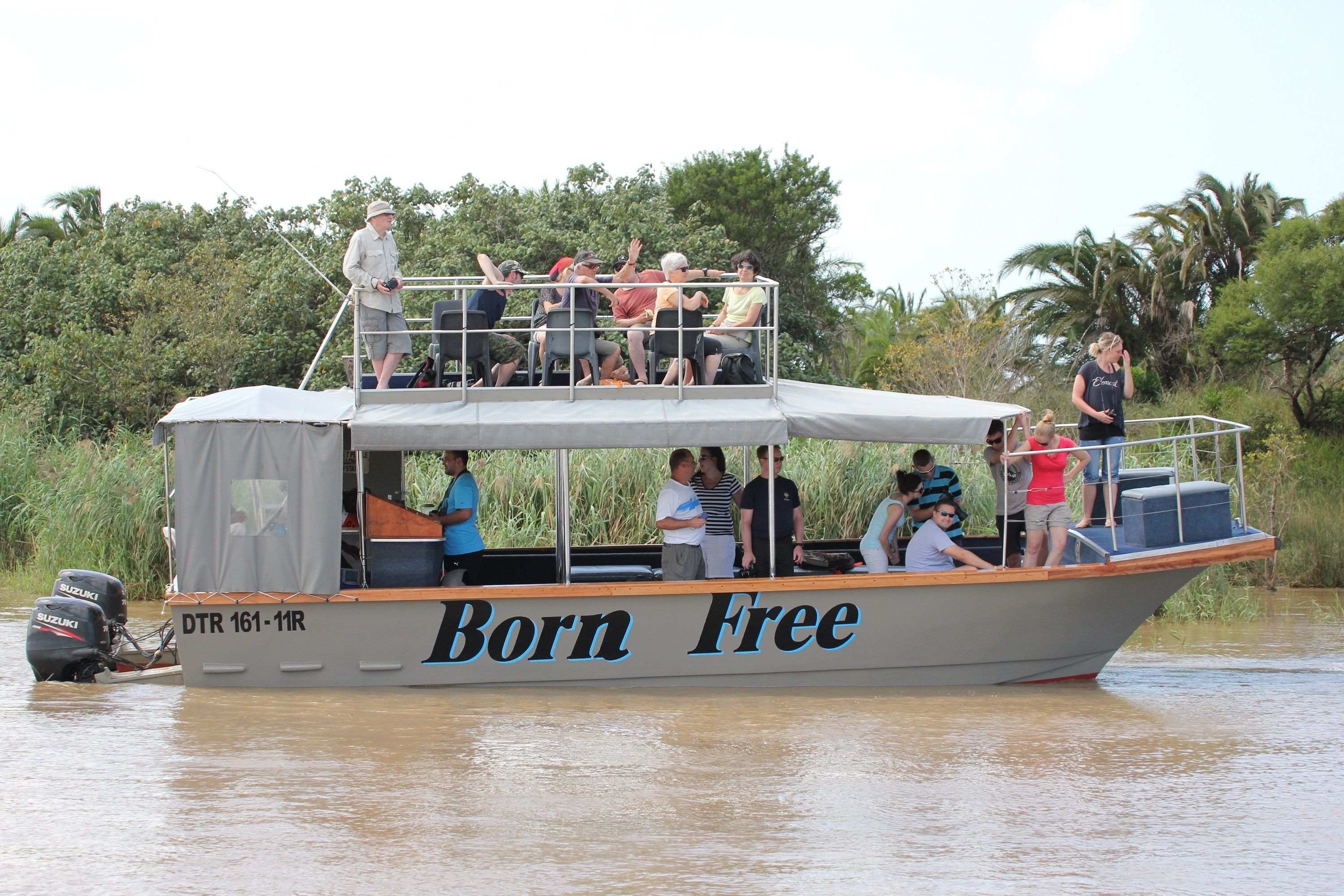 Un barco llamado 'Born Free' con pasajeros a bordo, rodeado de vegetación.