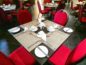 Un espace repas avec des chaises et des tables rouges, préparé pour un repas.