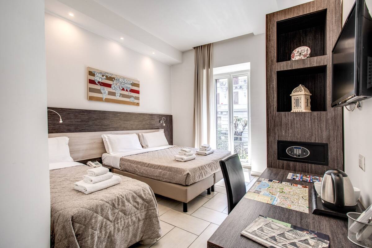 Una habitación de hotel con dos camas, un escritorio con un mapa, una cafetera y un televisor sobre una estantería de madera.