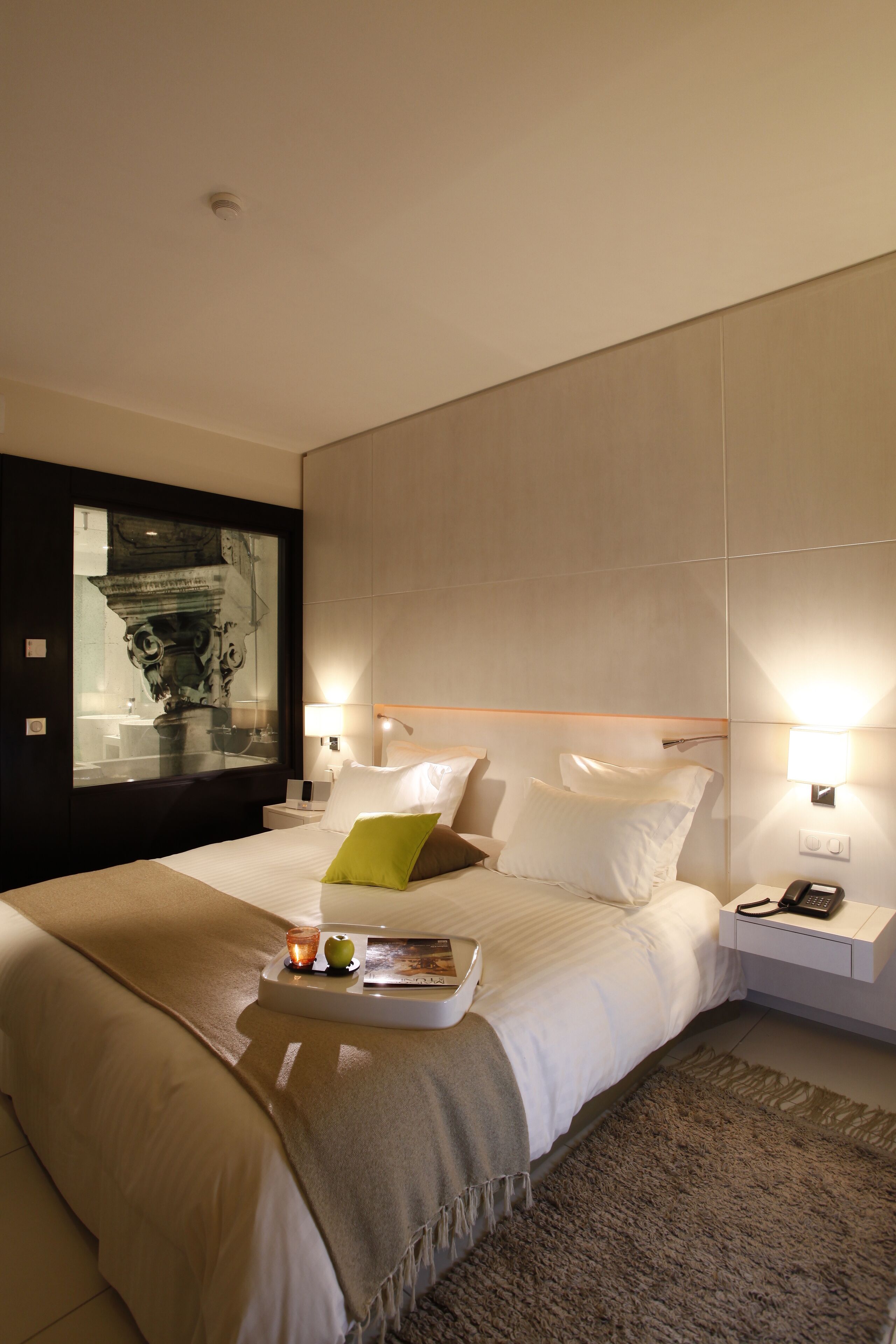 Una habitación de hotel moderna con una cama grande, una mesita de noche con lámpara y una obra de arte colgada en la pared.