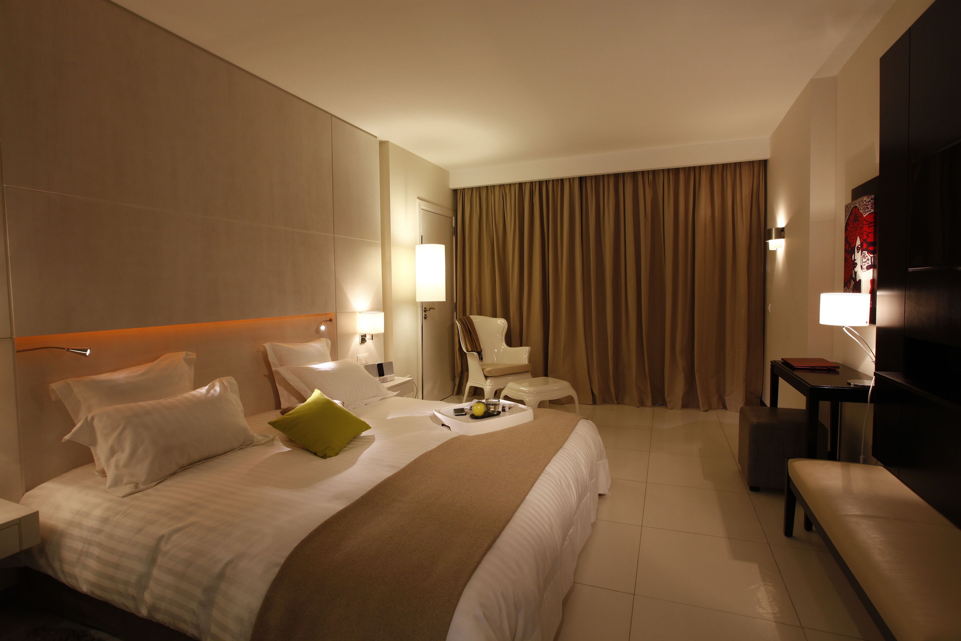 A hotel room with a large bed, a desk, a chair, a TV, and a window with curtains.