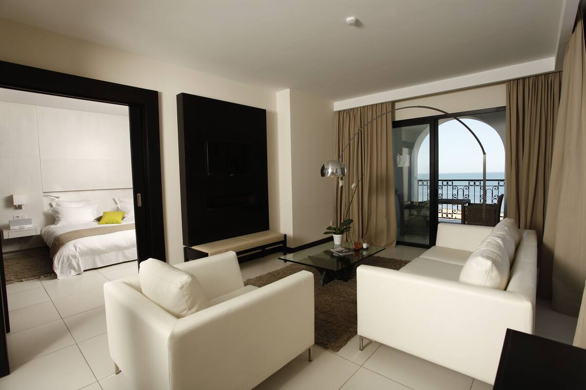 Una habitación de hotel moderna con balcón, muebles blancos y un televisor grande.