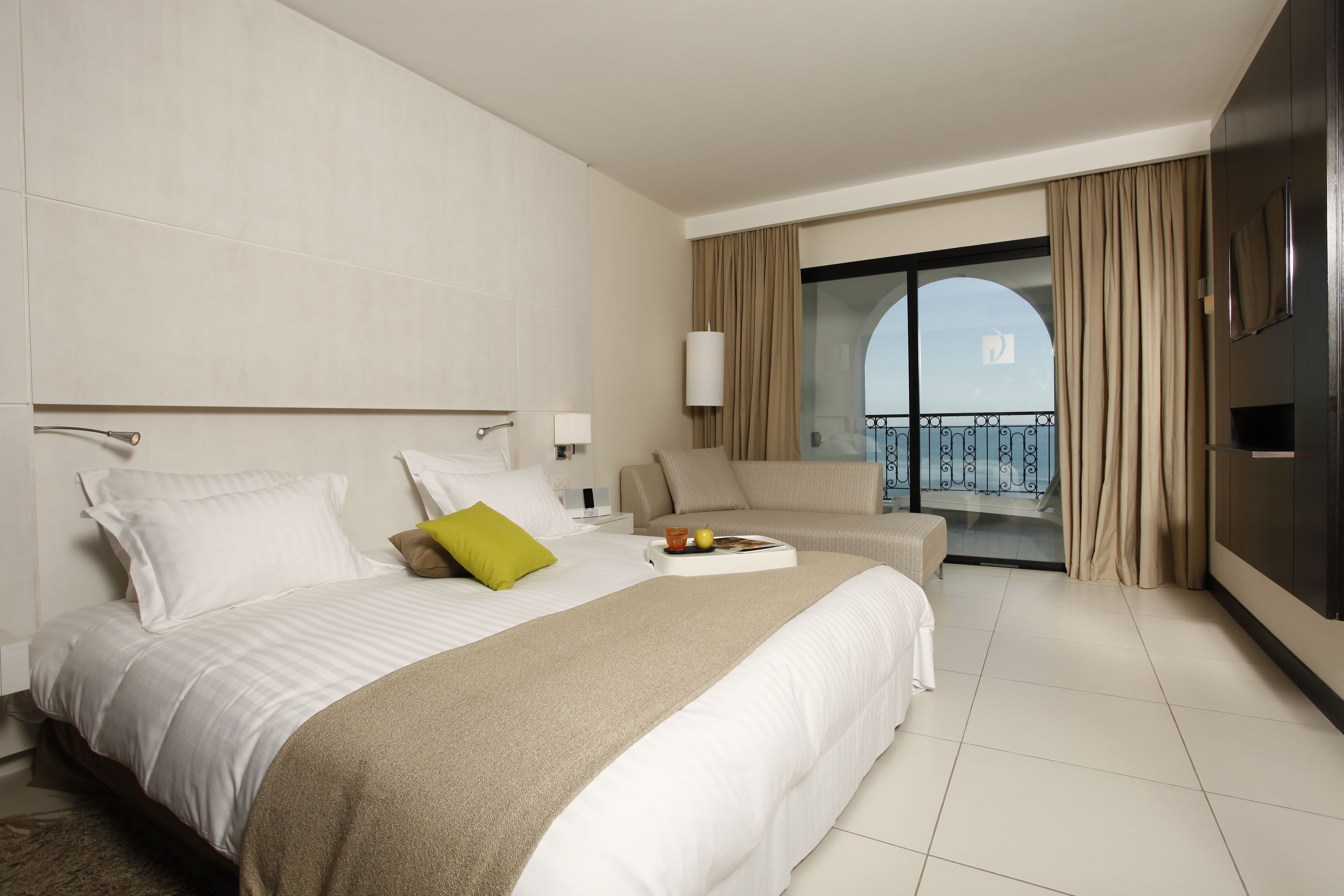 Een hotelkamer met een groot bed, een bank, een televisie en een balkon met gordijnen.