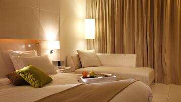 Una habitación de hotel con una cama, una mesita de noche, una lámpara, una bandeja con un vaso y una manzana, y cortinas color beige.