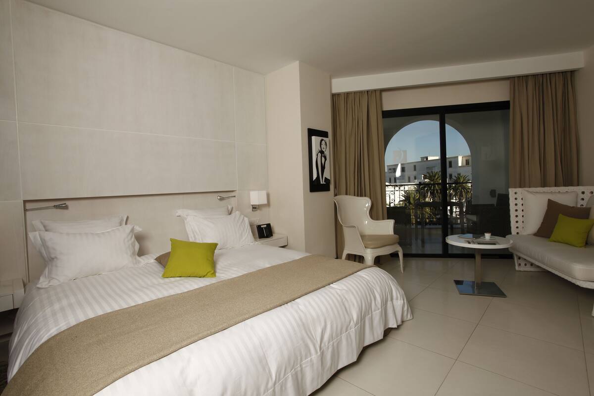 Habitación de hotel con una cama grande, un sofá, una silla, una mesita y vistas al exterior.