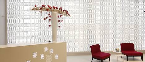 A reception area with a patterned wall, a reception desk, and two red chairs.