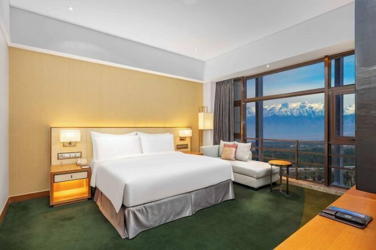 A hotel room with a large bed, a sofa, a small table, and a view of mountains.