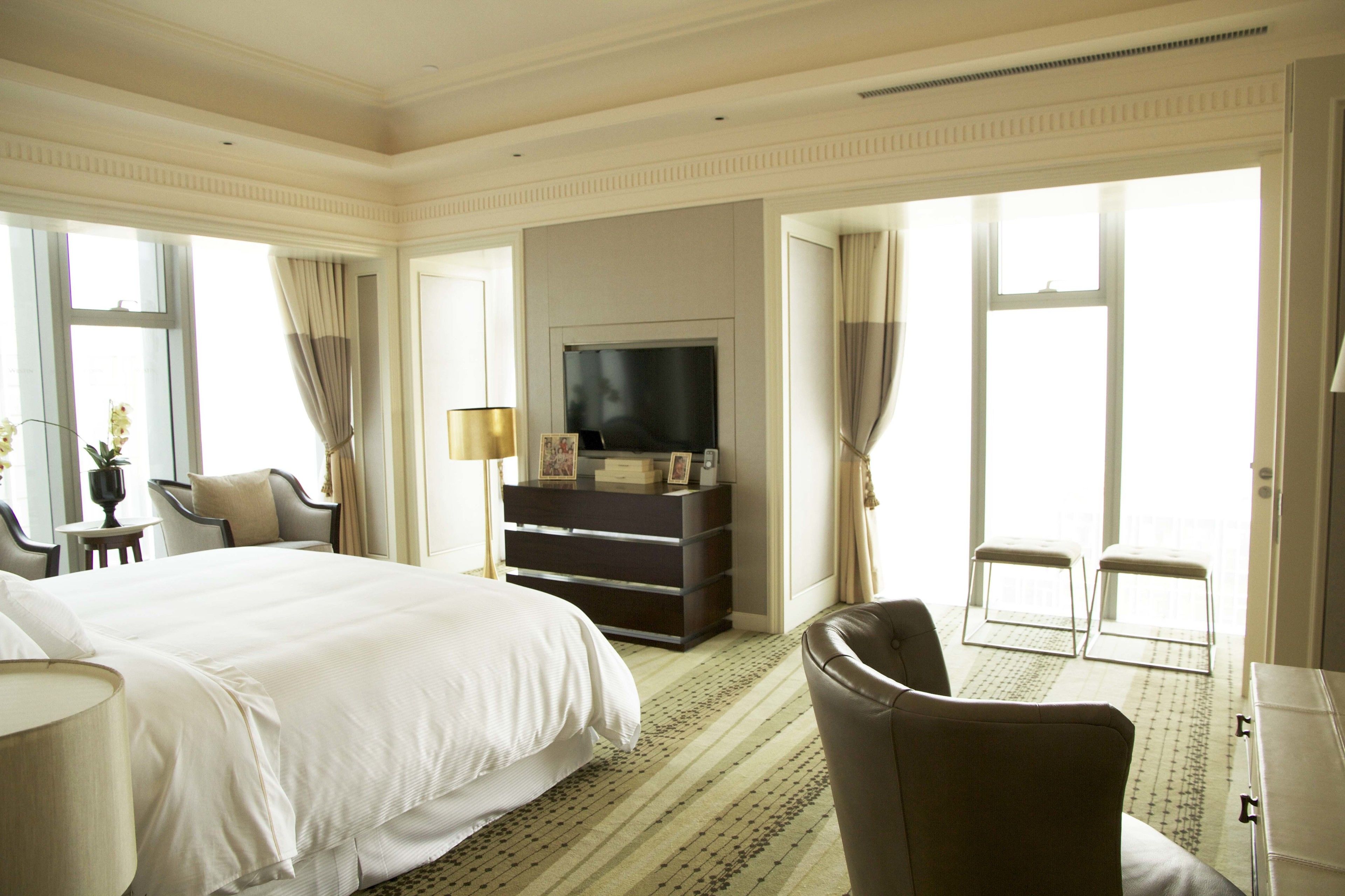 A hotel room with a large bed, a television, a dresser, and two chairs.