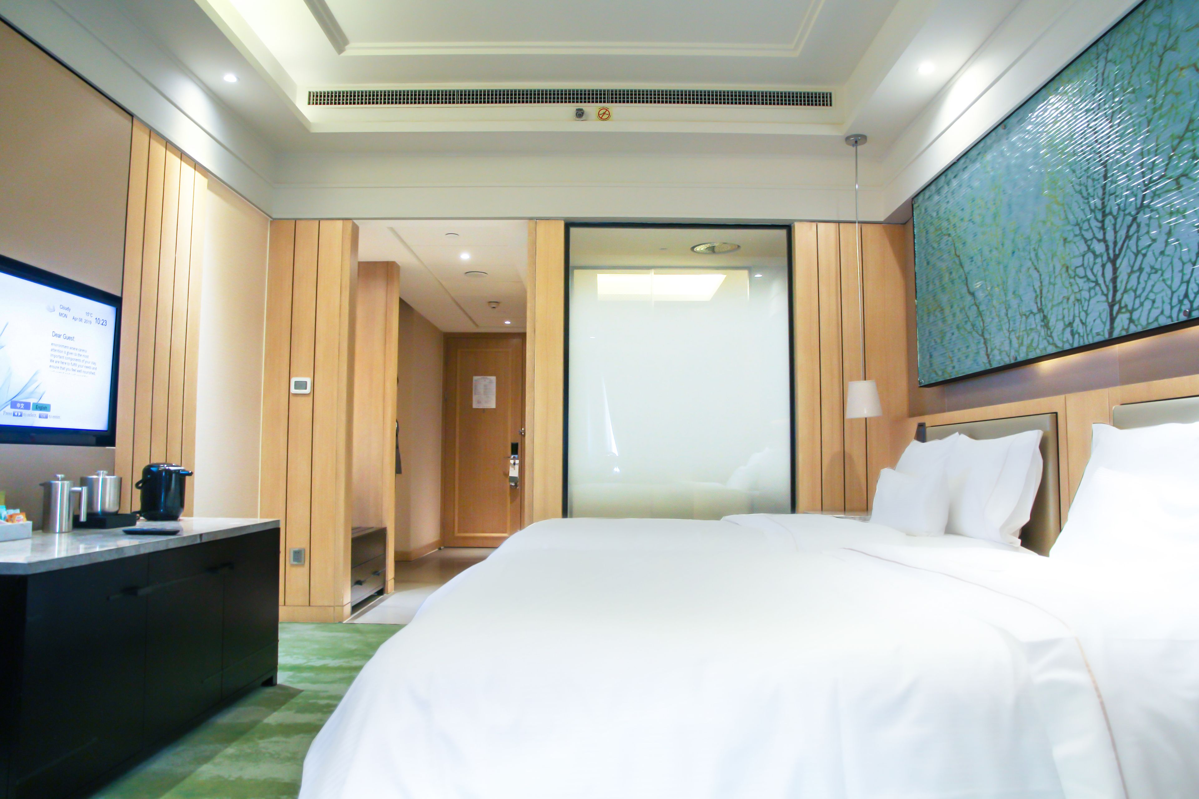 A hotel room with a large bed, a flat-screen TV, a desk with a coffee maker, and a painting on the wall.
