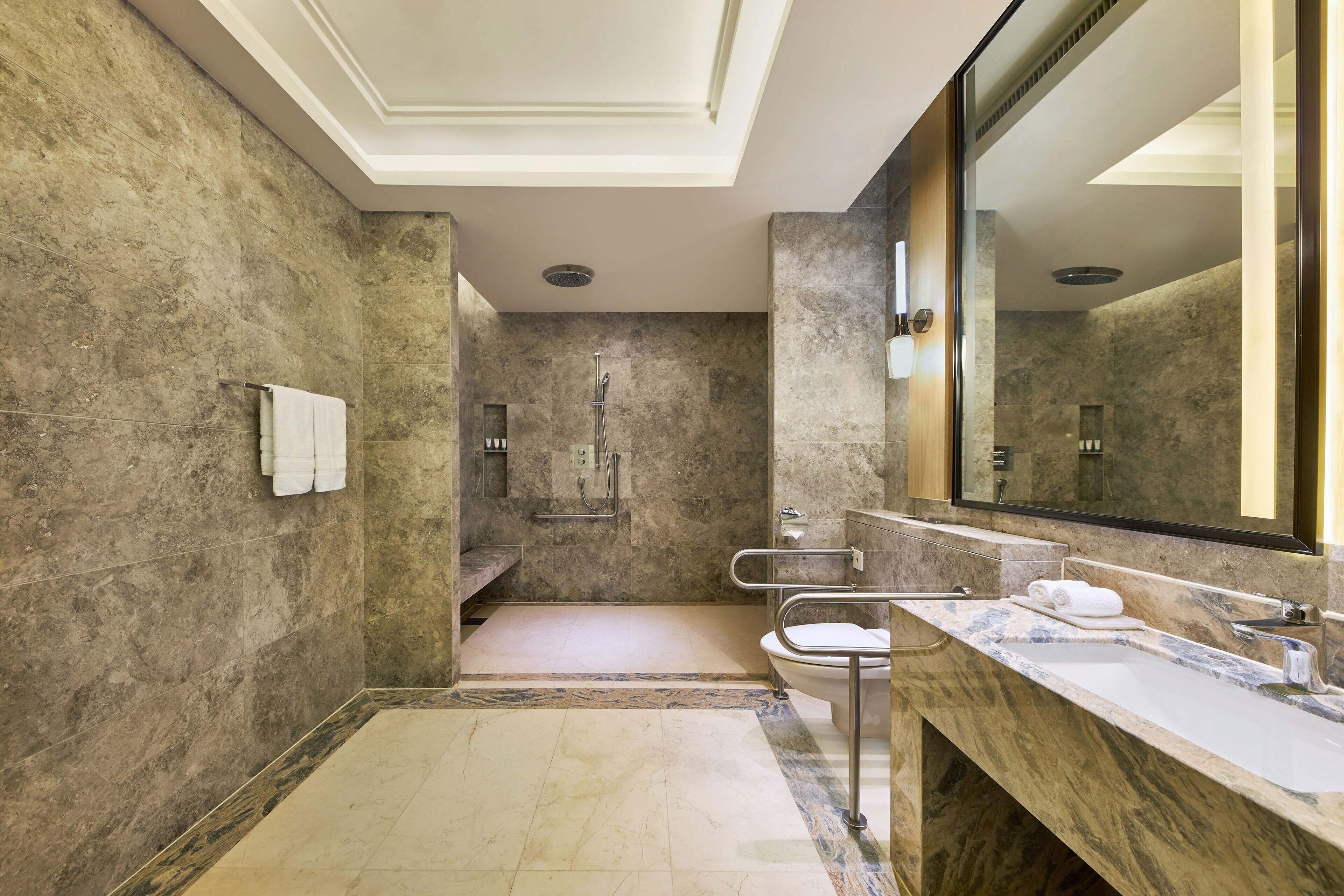 Ein modernes Badezimmer mit einem großen Spiegel, Marmorarbeitsplatten, einer Dusche und einer Toilette.