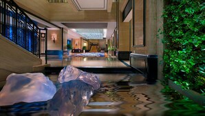 Un moderno vestíbulo de hotel con una escalera central, una zona de recepción y una escultura decorativa de hielo.