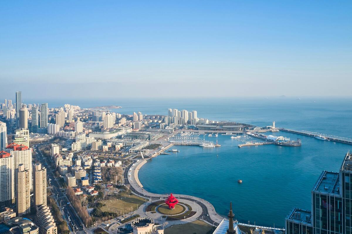 Un paysage urbain côtier avec de hauts immeubles, une marina et un monument rouge imposant.