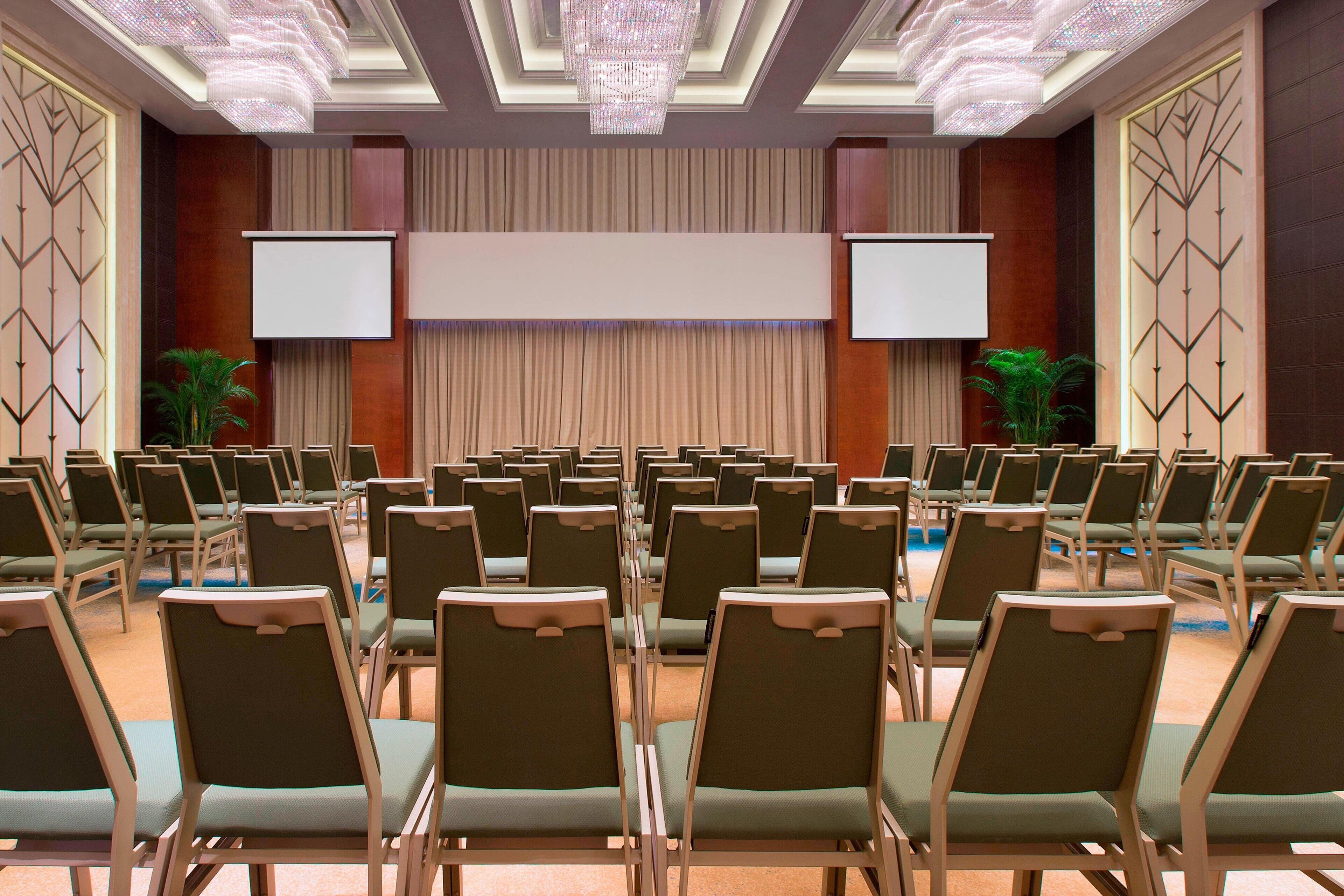 A conference room with rows of chairs, a large screen, and two projection screens.