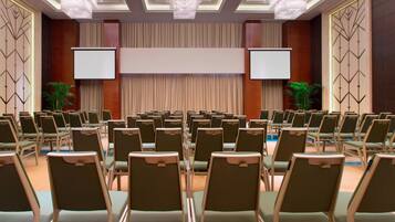 A conference room with rows of chairs, a large screen, and two projection screens.