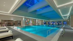 A large indoor swimming pool with a skylight ceiling, lounge chairs with towels, and a modern interior design. - The Westin Qingdao (Qingdao)