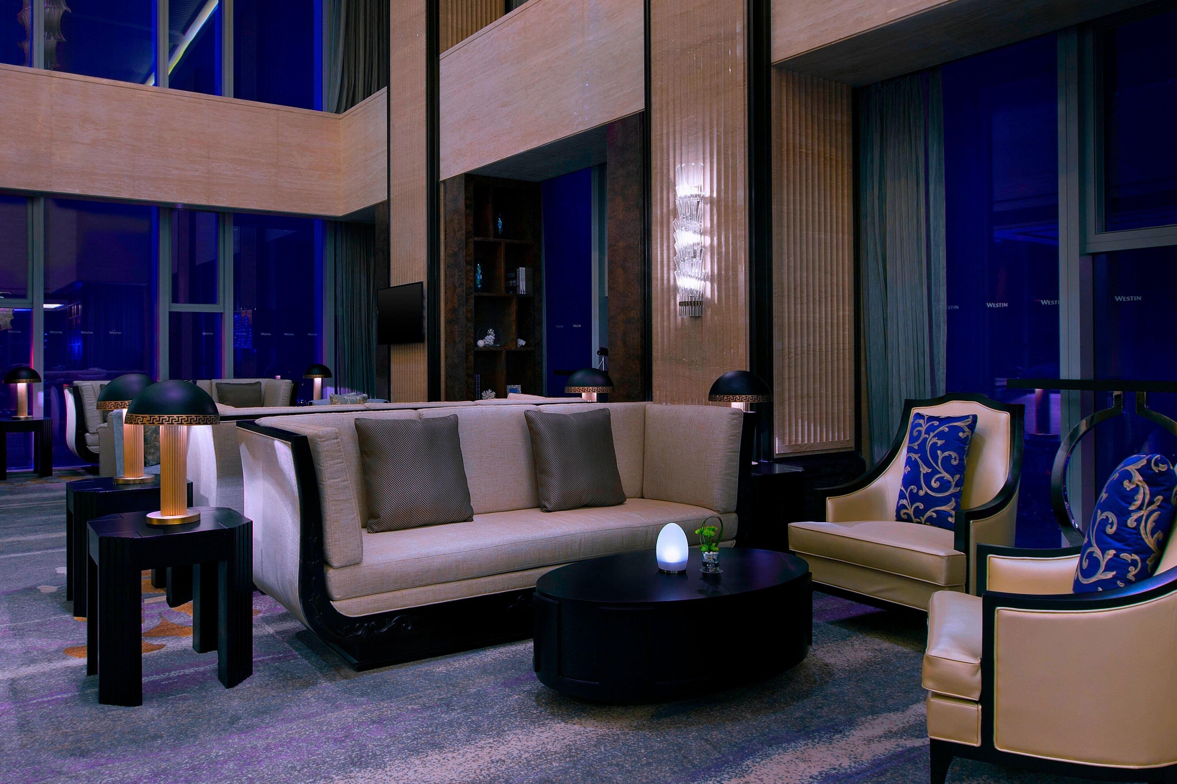 A modern hotel lobby with a sofa, armchairs, a coffee table, and a bookshelf.