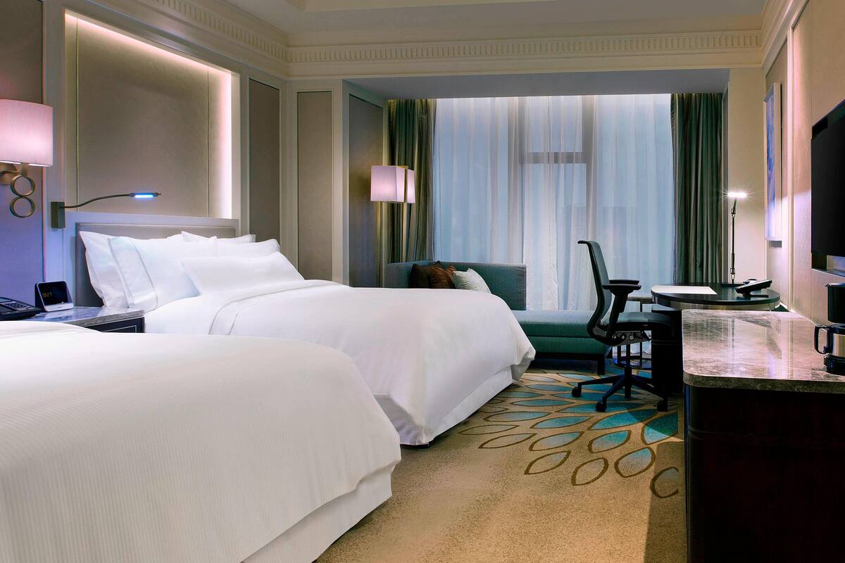 Une chambre d’hôtel avec deux lits, un bureau avec une chaise, une télévision et une fenêtre avec des rideaux.