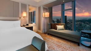 A hotel room with a large bed, a sofa, a desk, and a view of the city at sunset. - The Westin Qingdao (Qingdao)