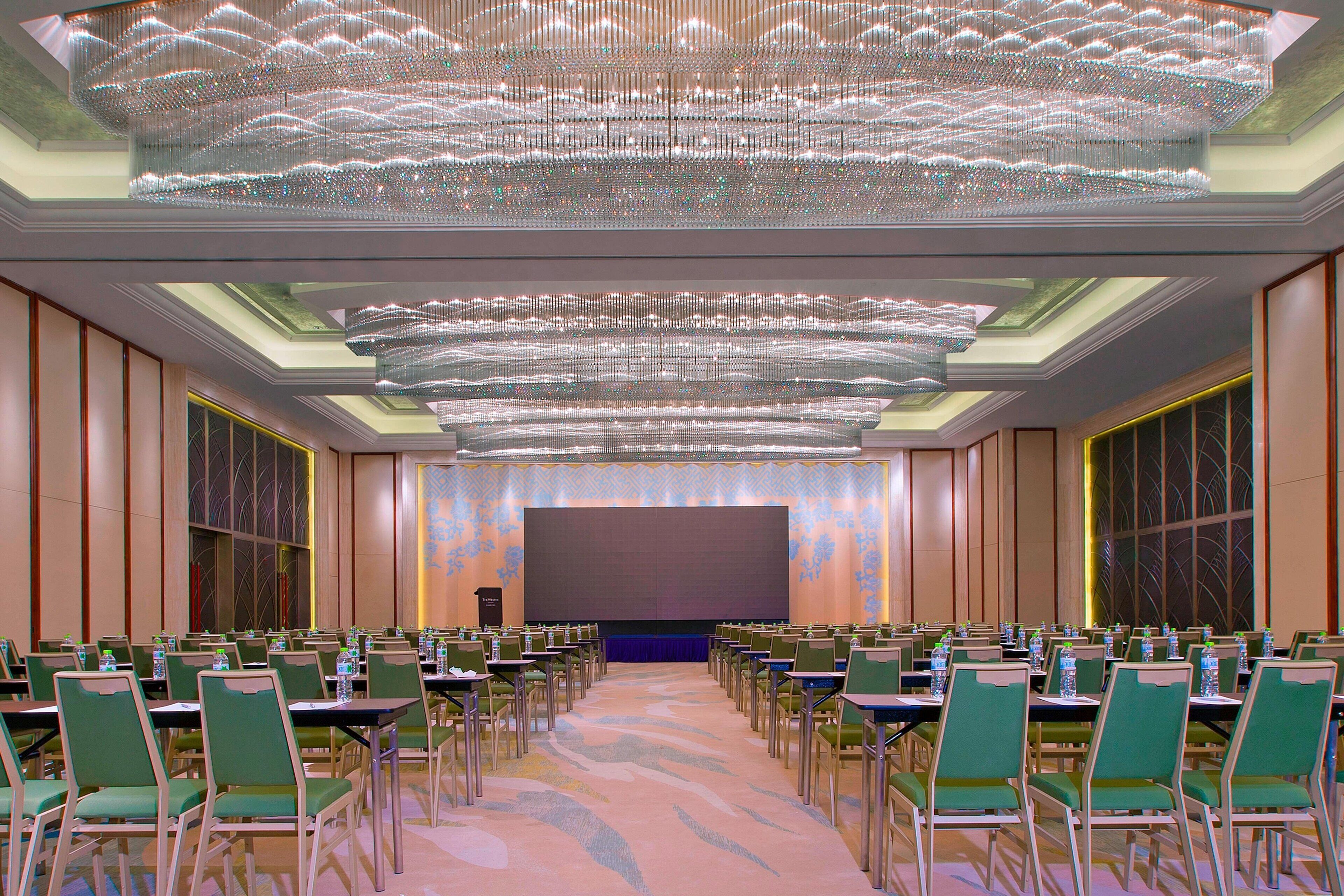 Un salón de conferencias con filas de sillas verdes, una pantalla grande y una araña.