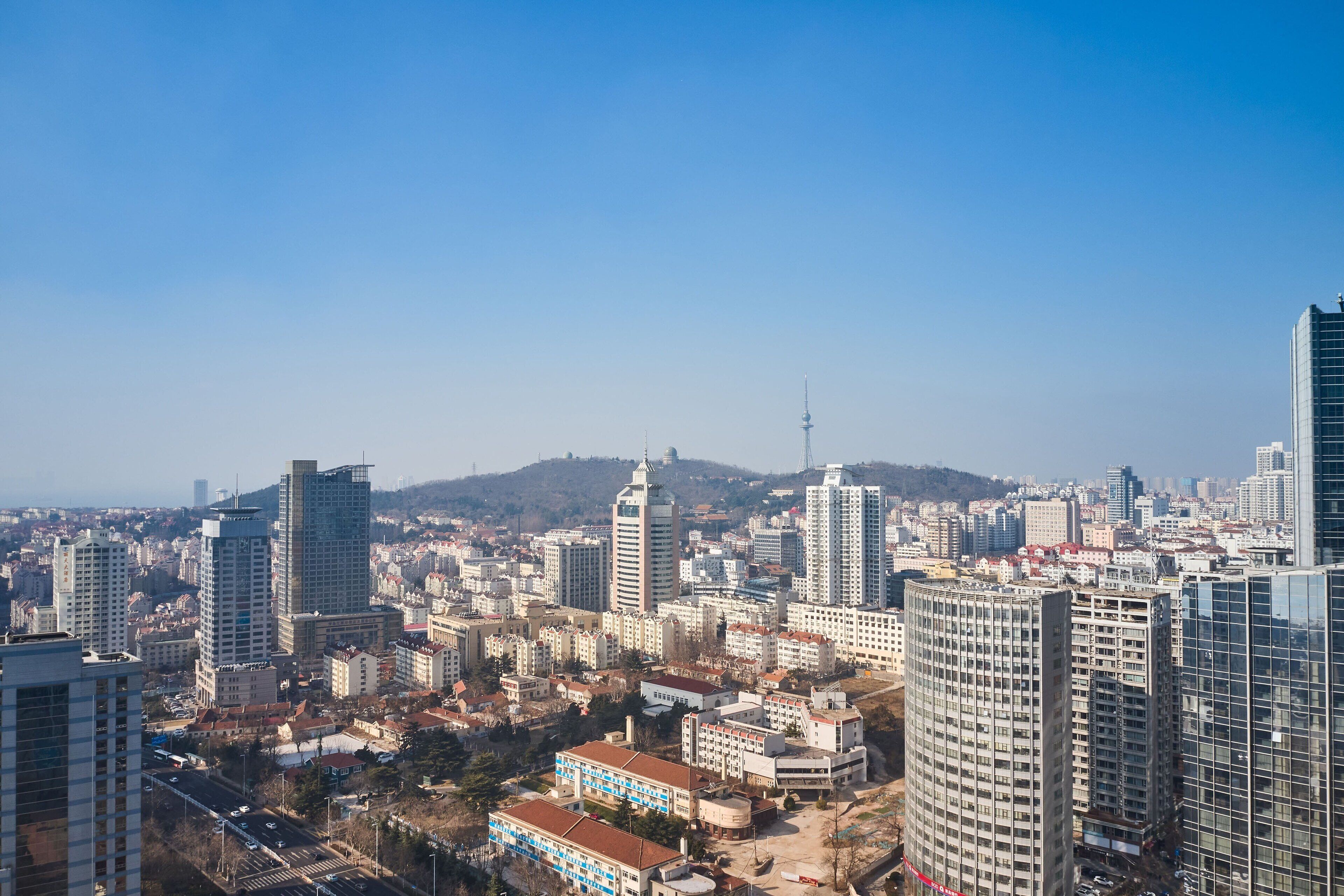 A cityscape with high-rise buildings, a prominent tower, and a hilly background.