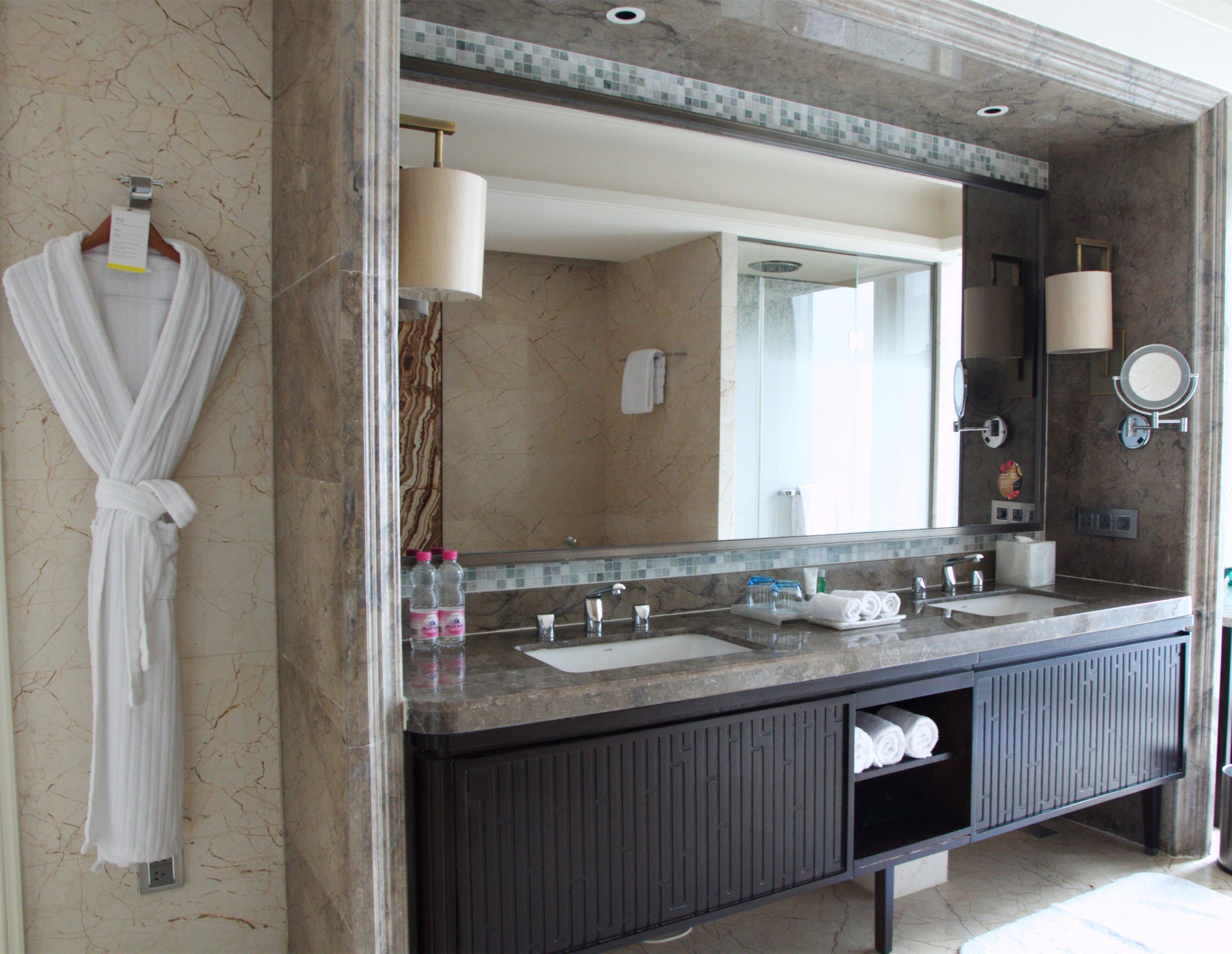 A bathroom with a marble vanity, two sinks, a large mirror, and a robe hanging on the wall.