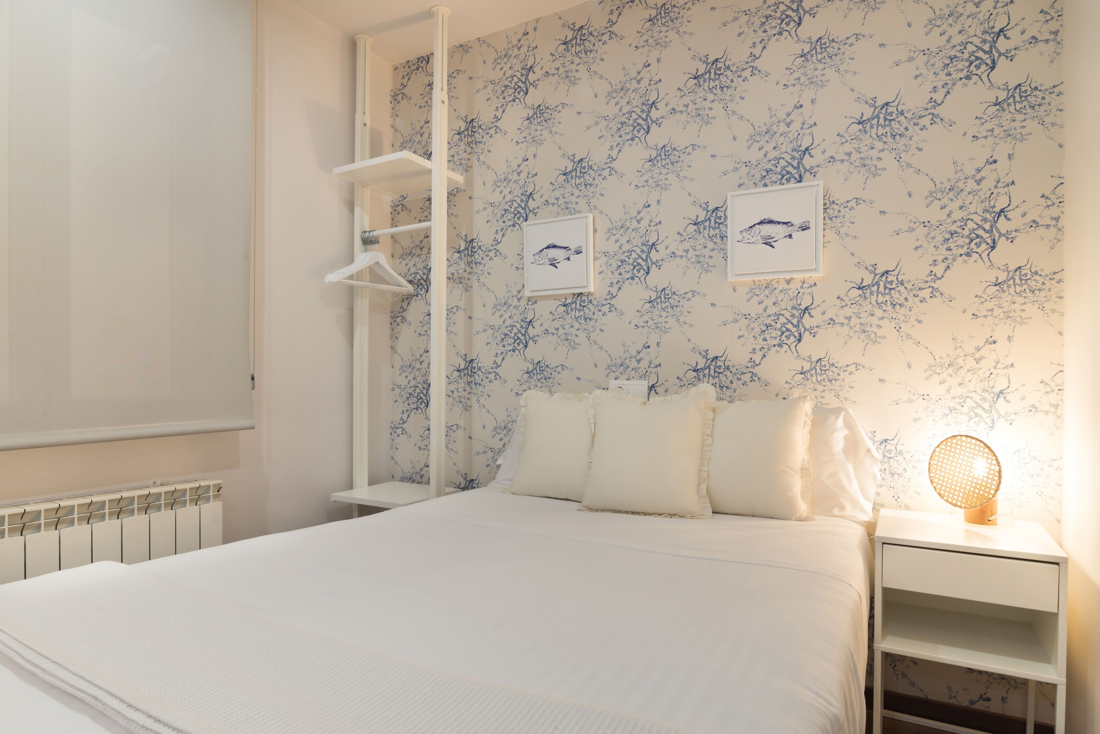 Een slaapkamer met een bed, witte nachtkastjes, een wandplank en een radiator.