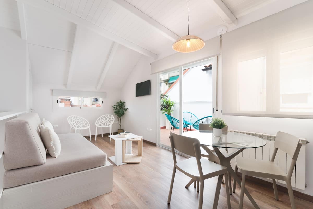 A modern living room with a sofa, a glass table, and chairs. There is a TV on the wall and a plant on the table.