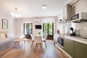 A modern kitchen with a dining area, a sofa, and a TV.