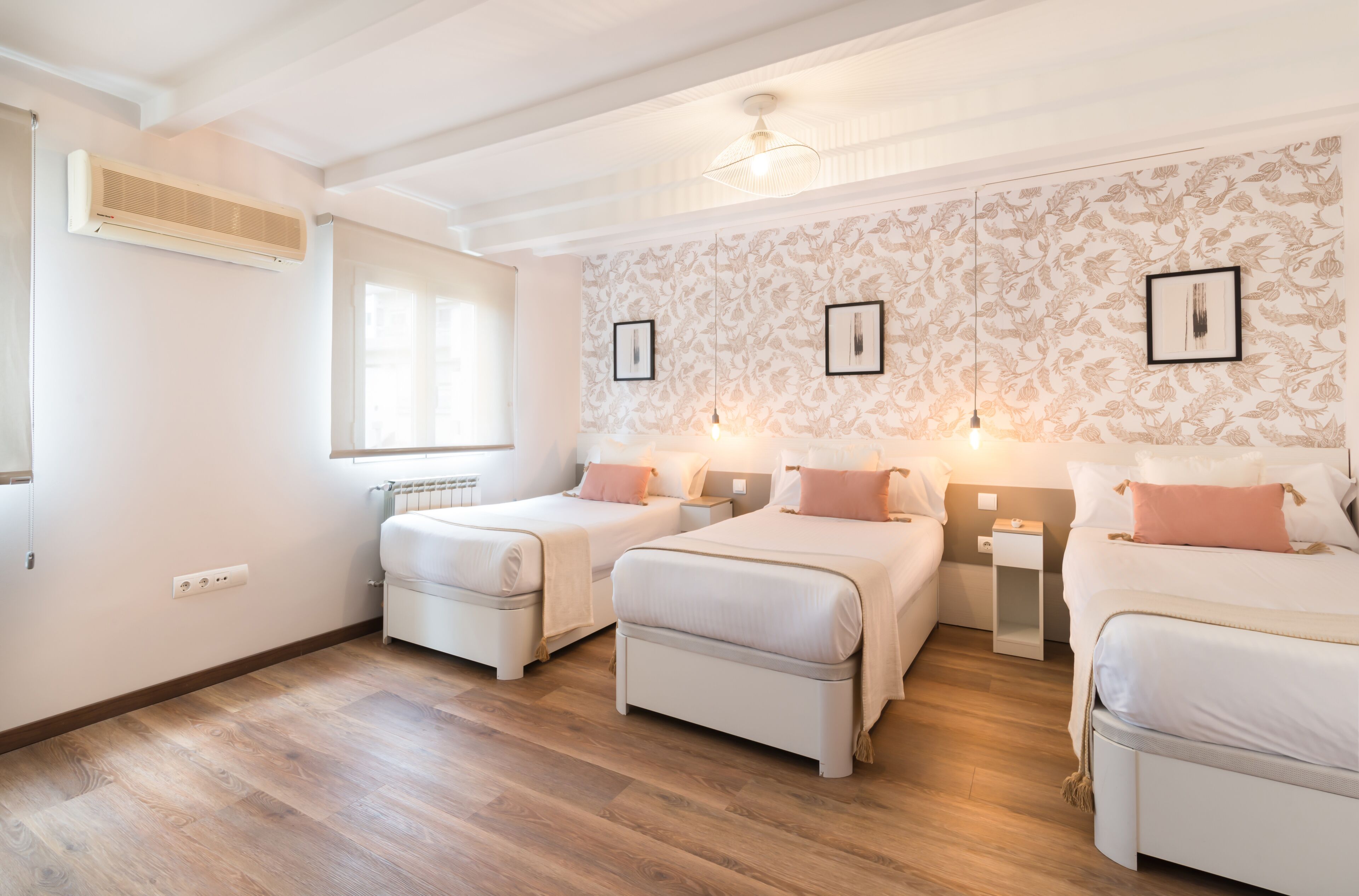 Une chambre d’hôtel avec deux lits, une fenêtre, un climatiseur et un mur orné de tableaux.
