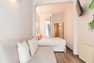 A modern bedroom with a sofa bed, a flat-screen TV mounted on the wall, and a radiator.