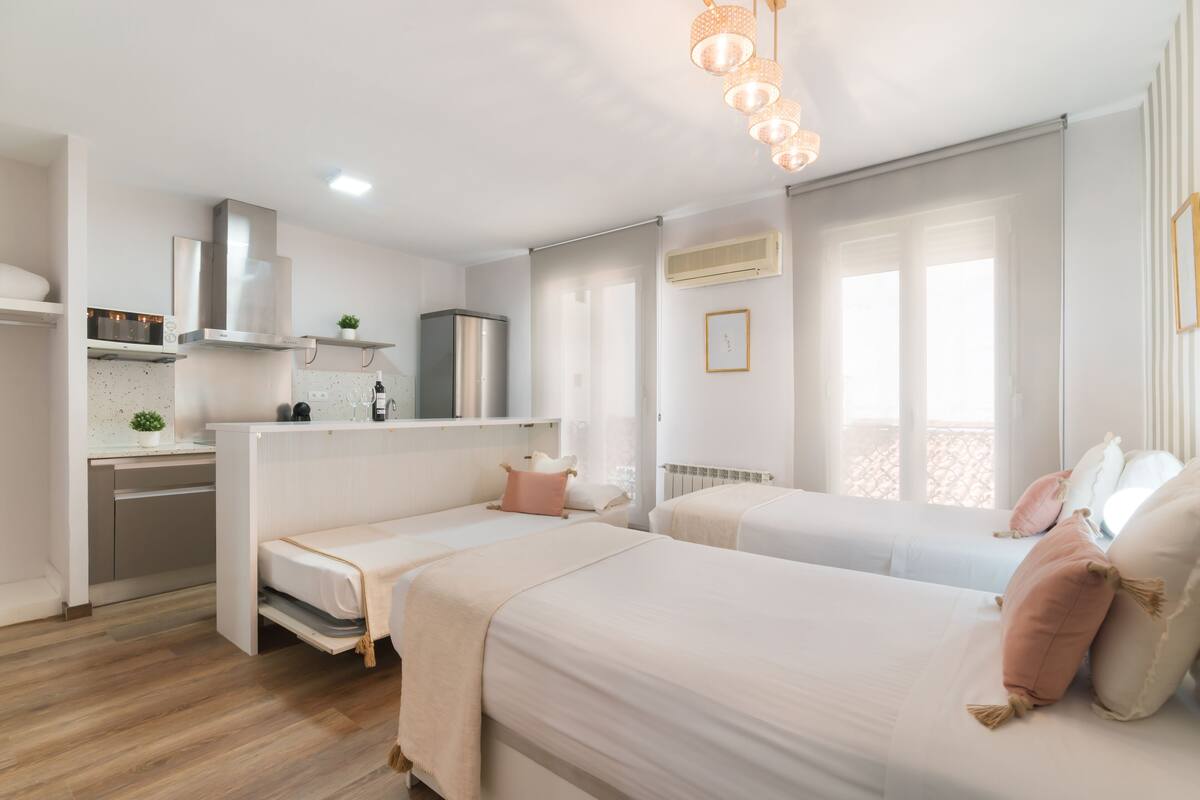 A modern bedroom with two beds, a kitchenette, and a balcony.