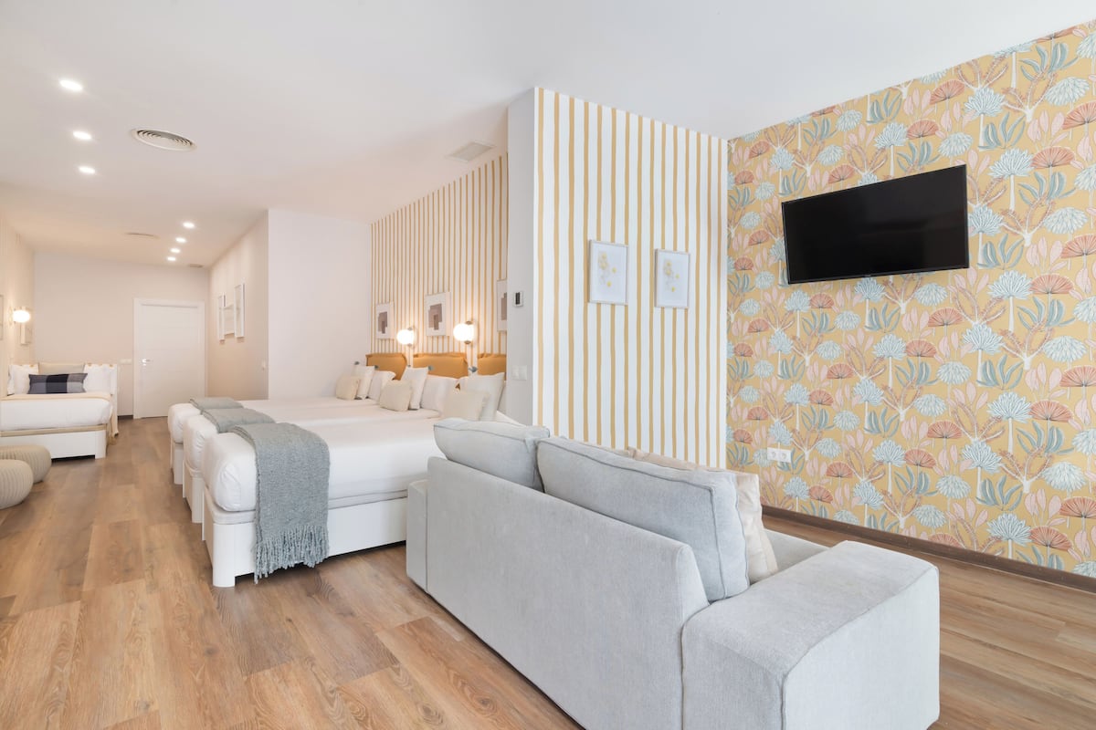 A modern hotel room with a large bed, a sofa, and a television mounted on the wall.