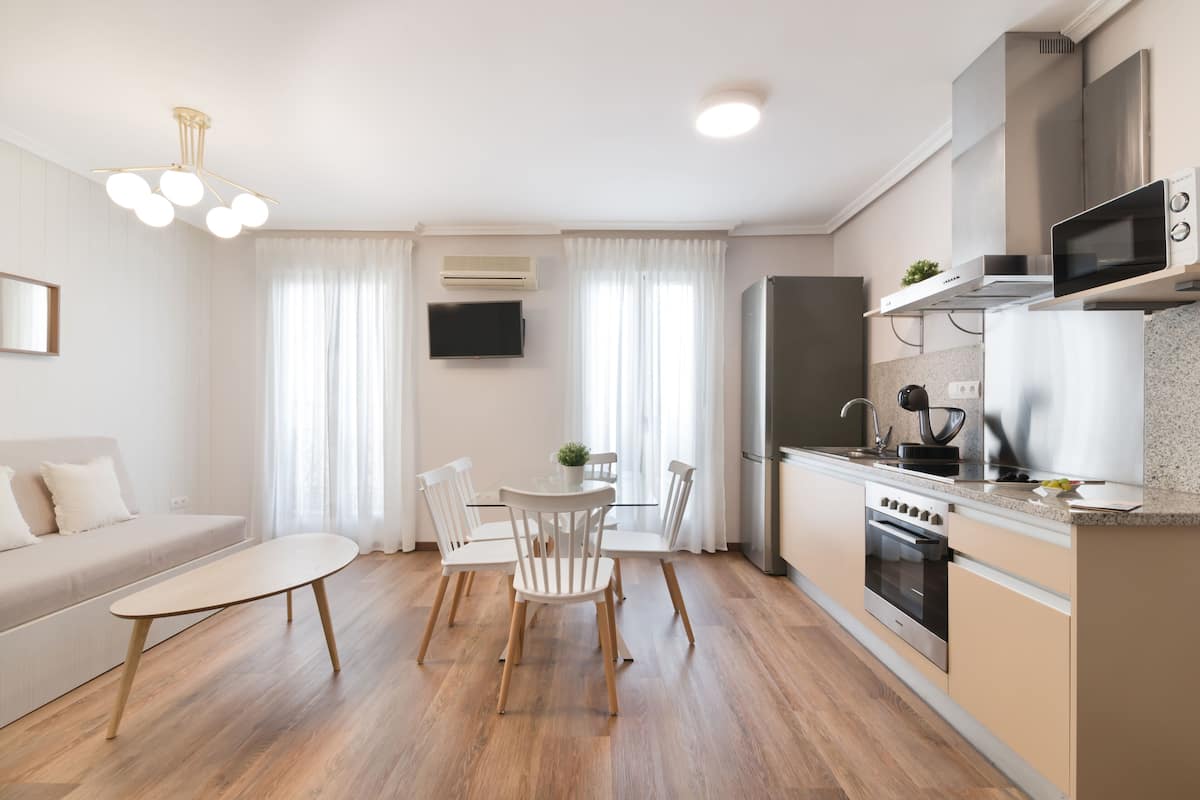 A modern kitchen with a built-in oven, microwave, and stove. There is a dining table with chairs and a small potted plant.