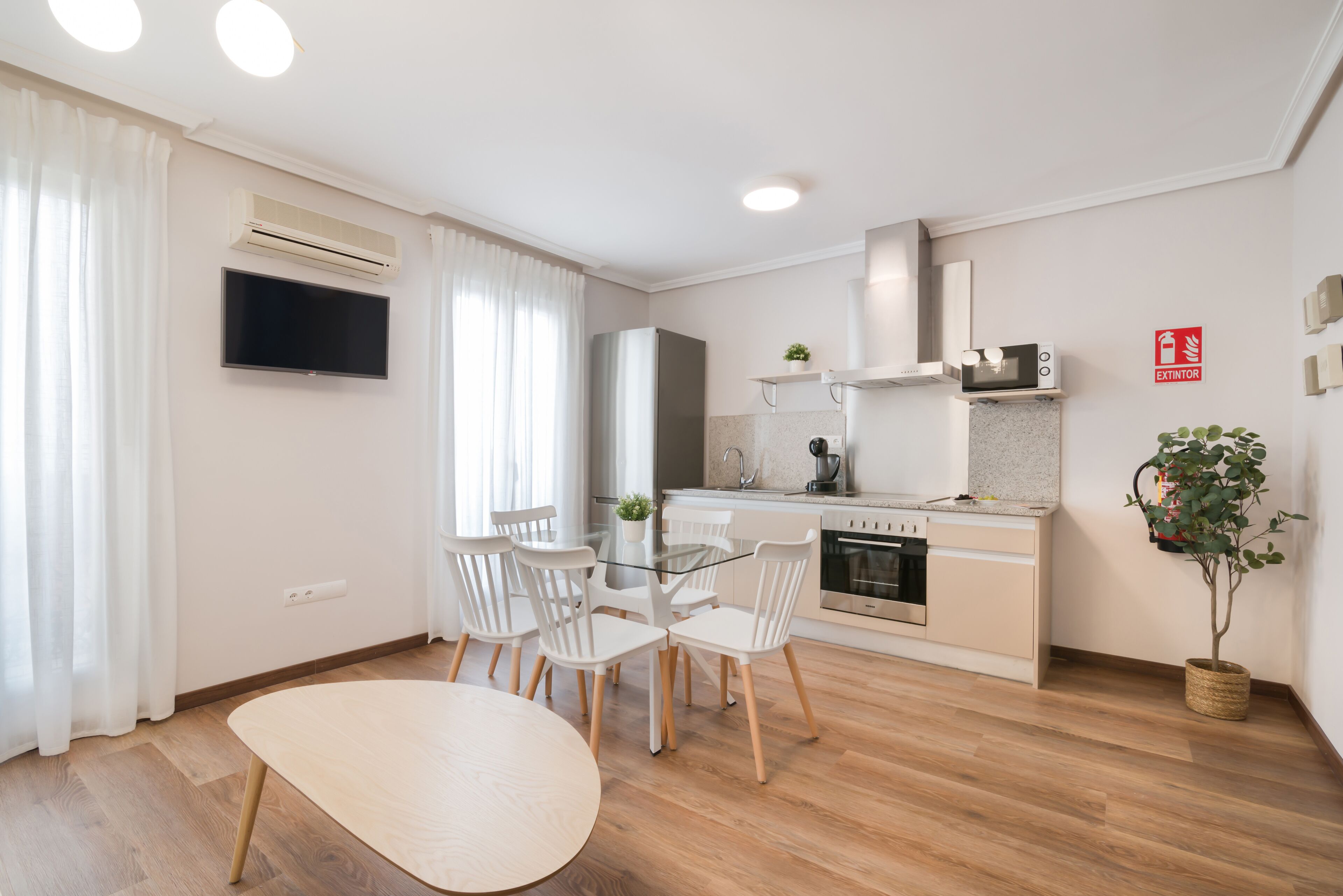 A modern kitchen with a microwave, stove, and sink. There is a dining area with a glass table and white chairs.