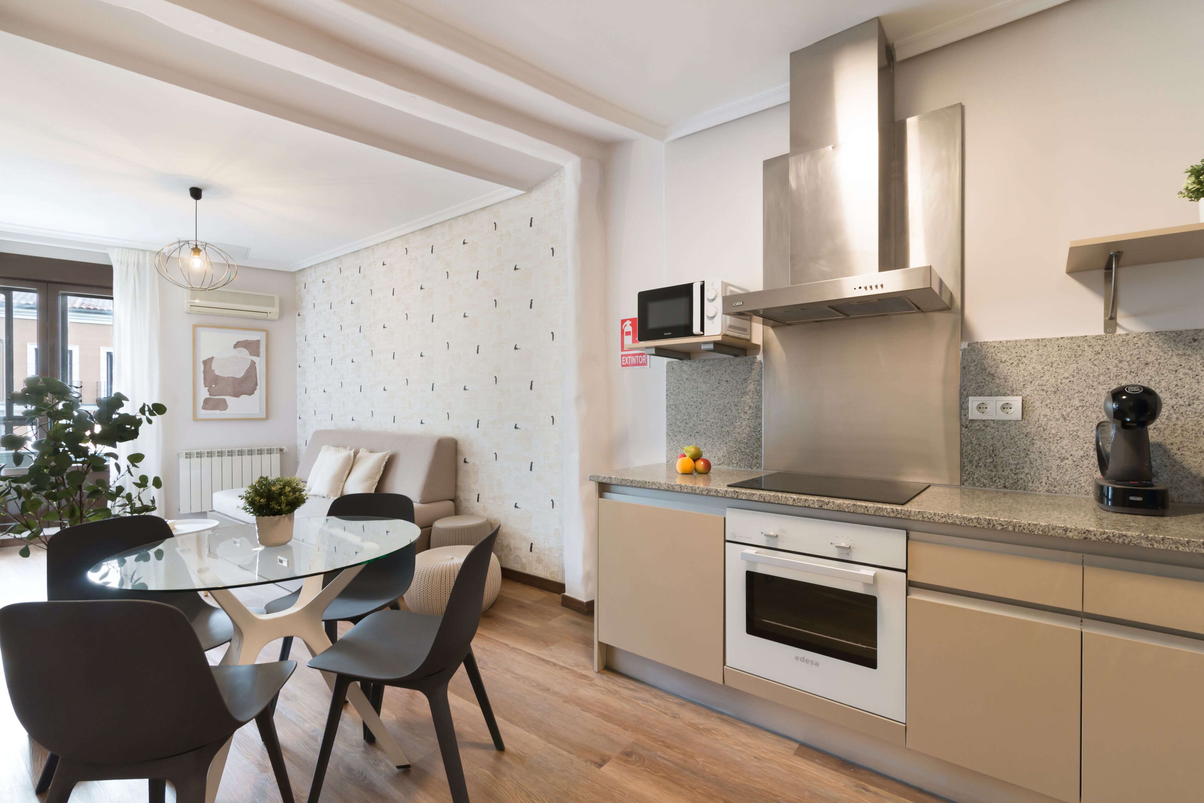 A modern kitchen with a glass dining table, beige cabinetry, and a stainless steel range hood.