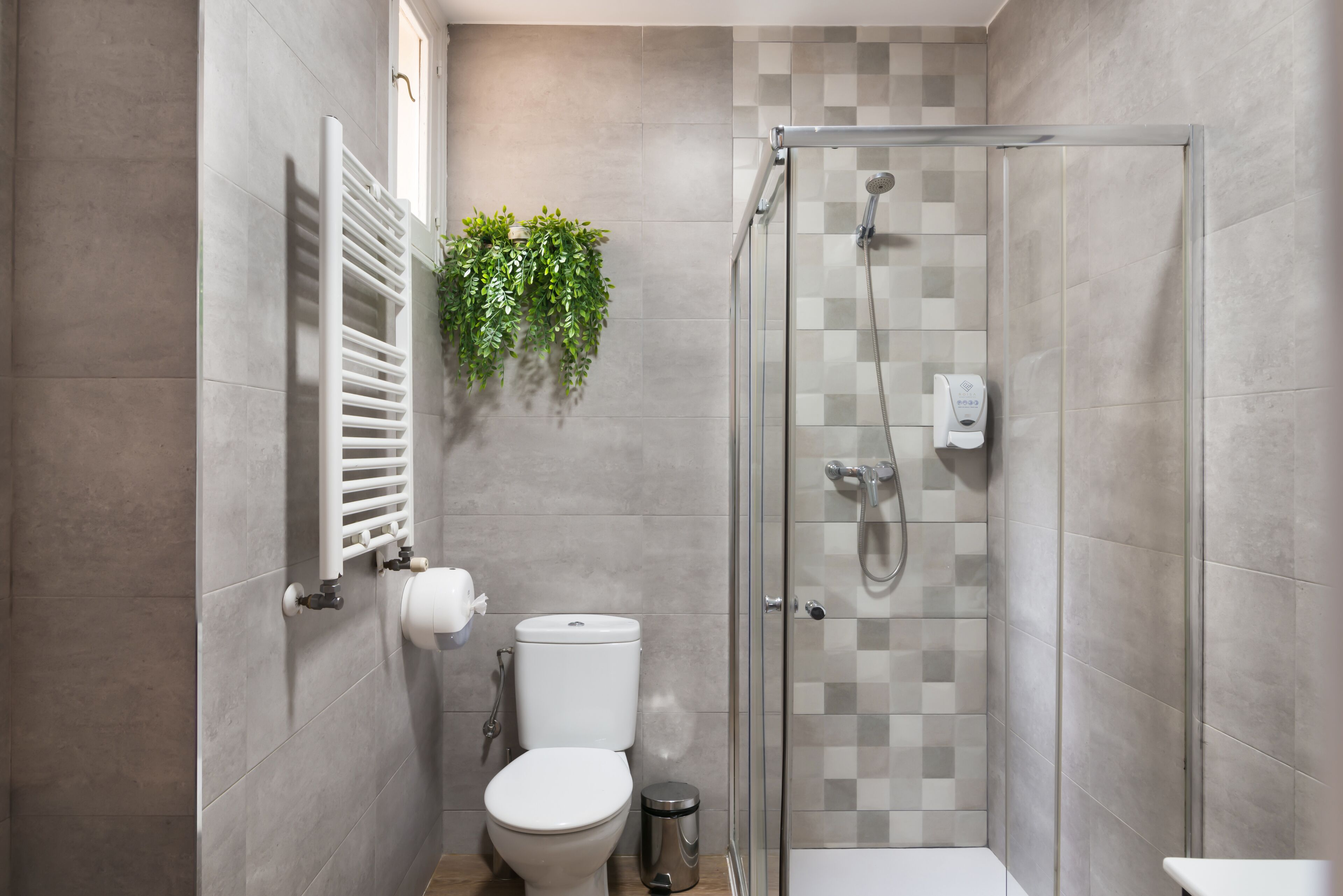 Een moderne badkamer met een douchecabine van glas, een toilet, een radiator en een hangplant.
