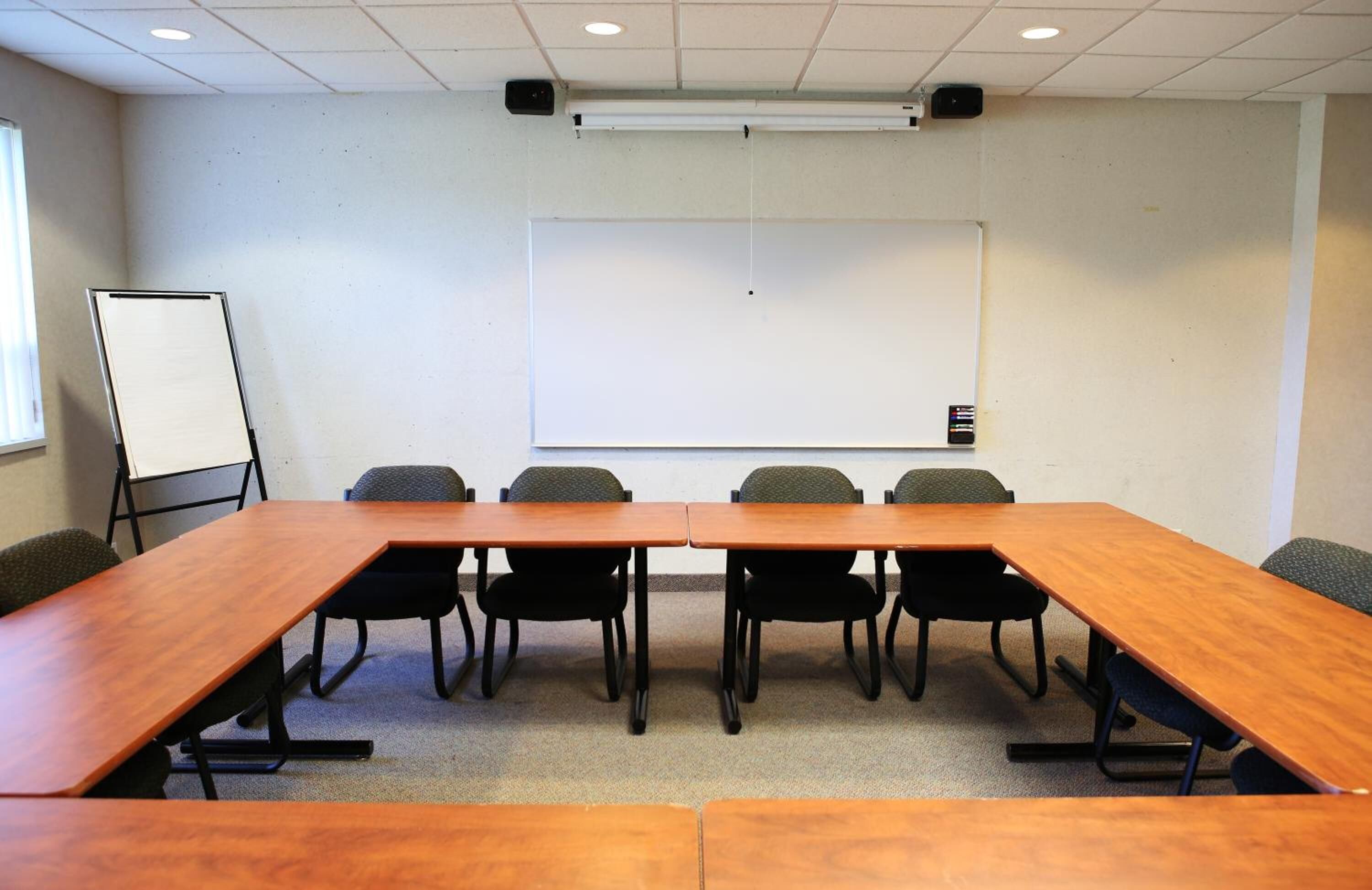 A conference room with a long table, six chairs, a whiteboard, and a projector.