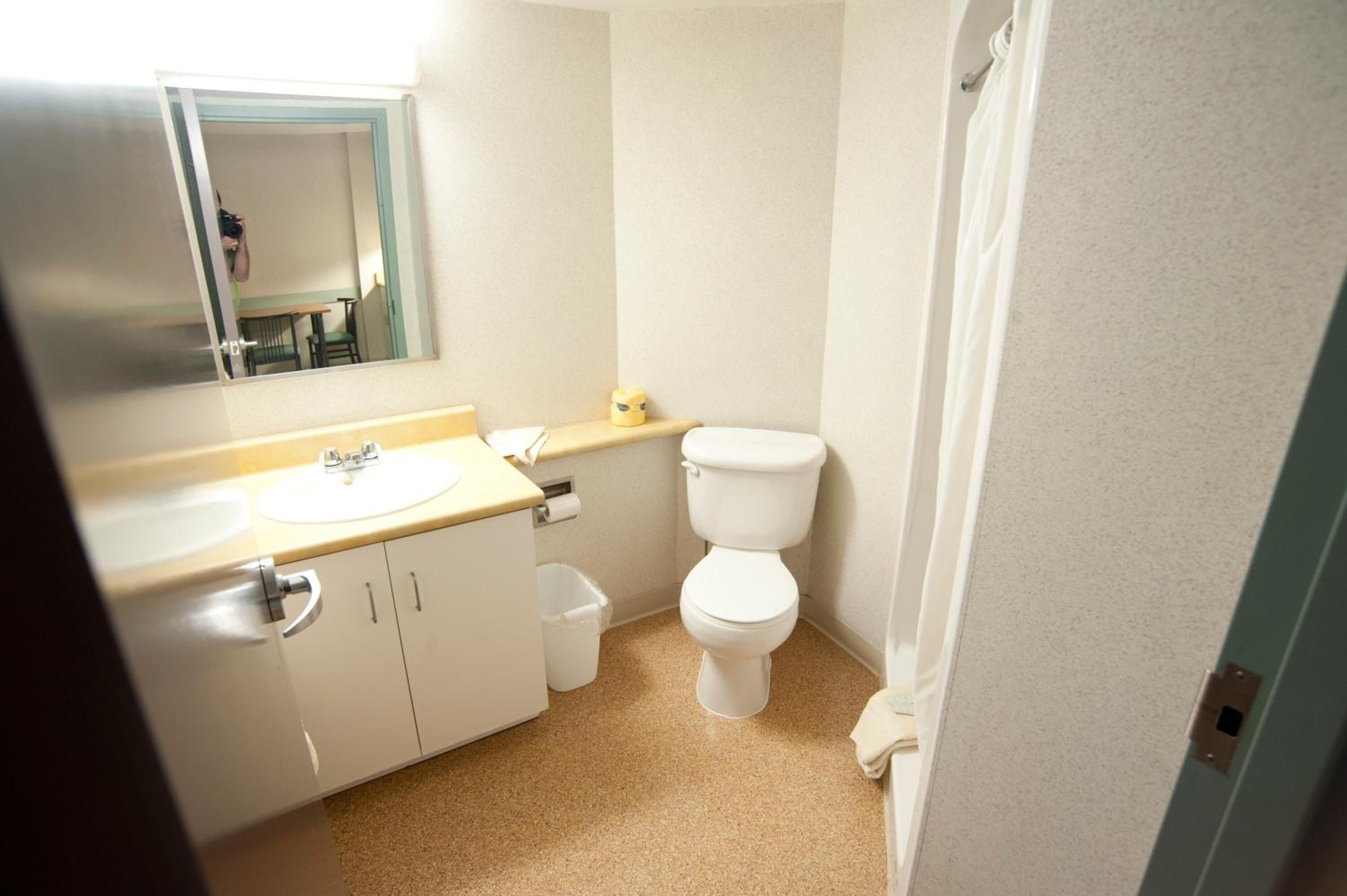 A small, clean bathroom with a sink, mirror, toilet, and a small trash bin.