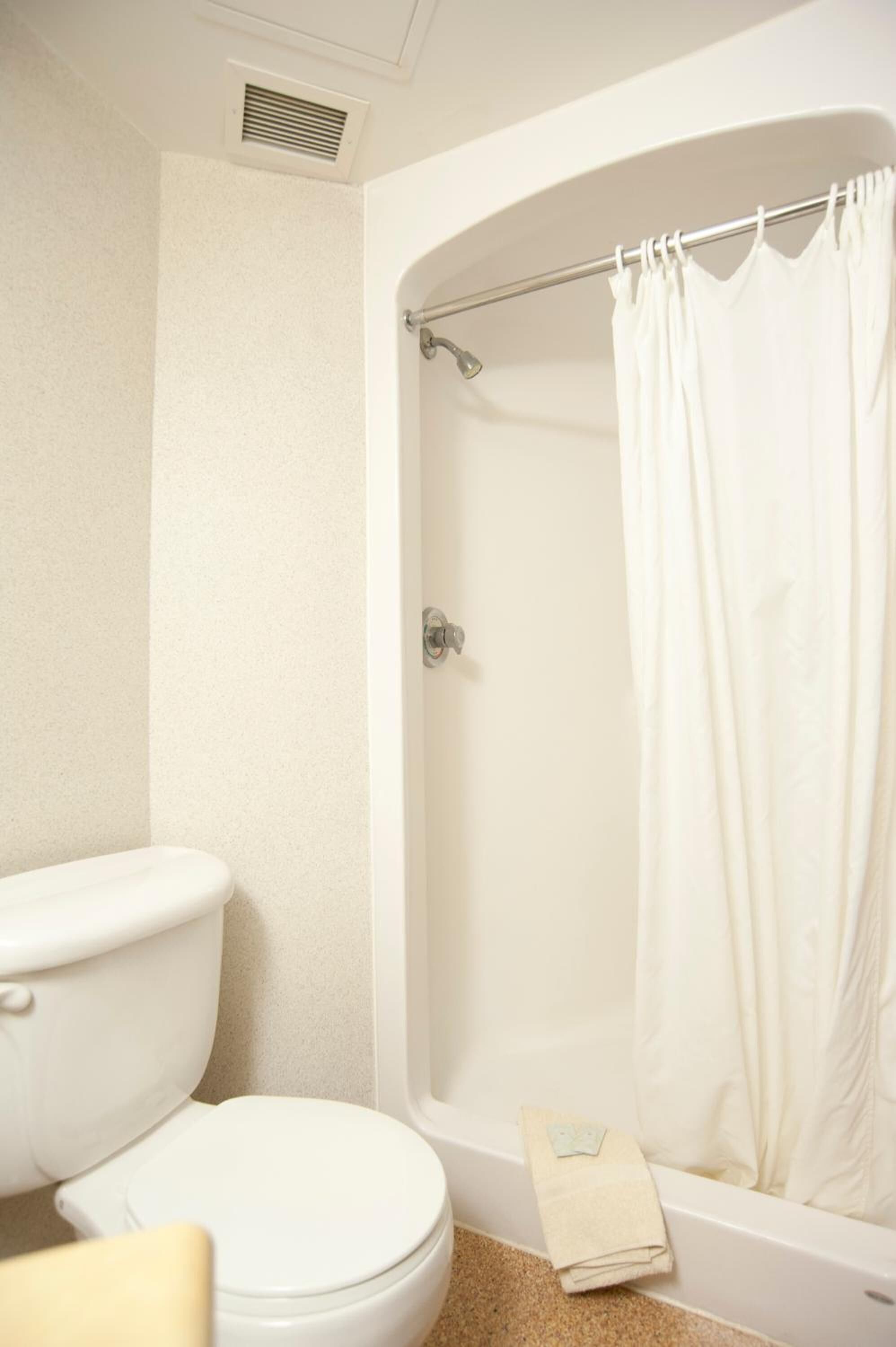 A bathroom with a toilet, a shower, and a towel on the floor.