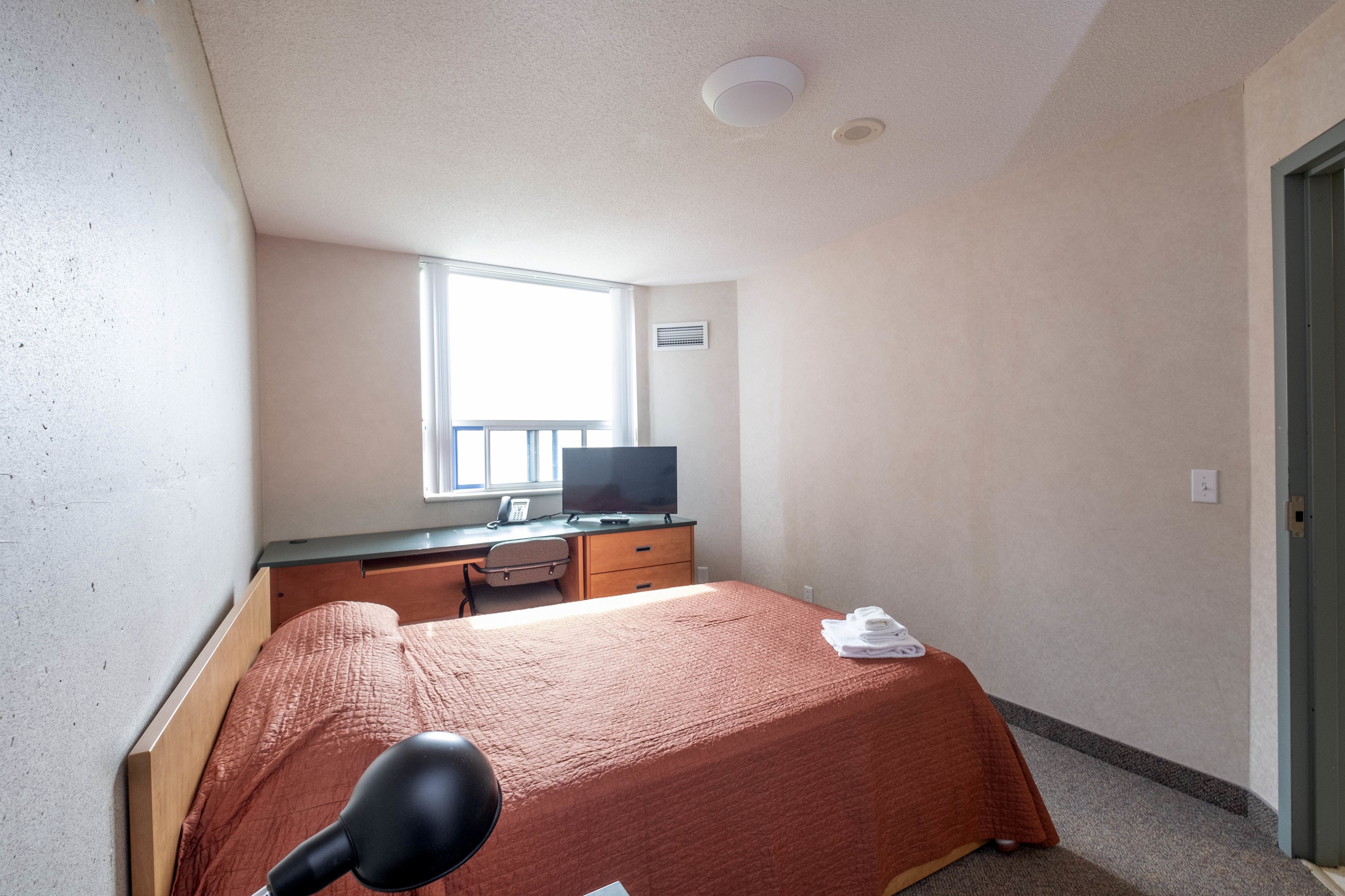 A bedroom with a bed, a desk, a television, and a window.