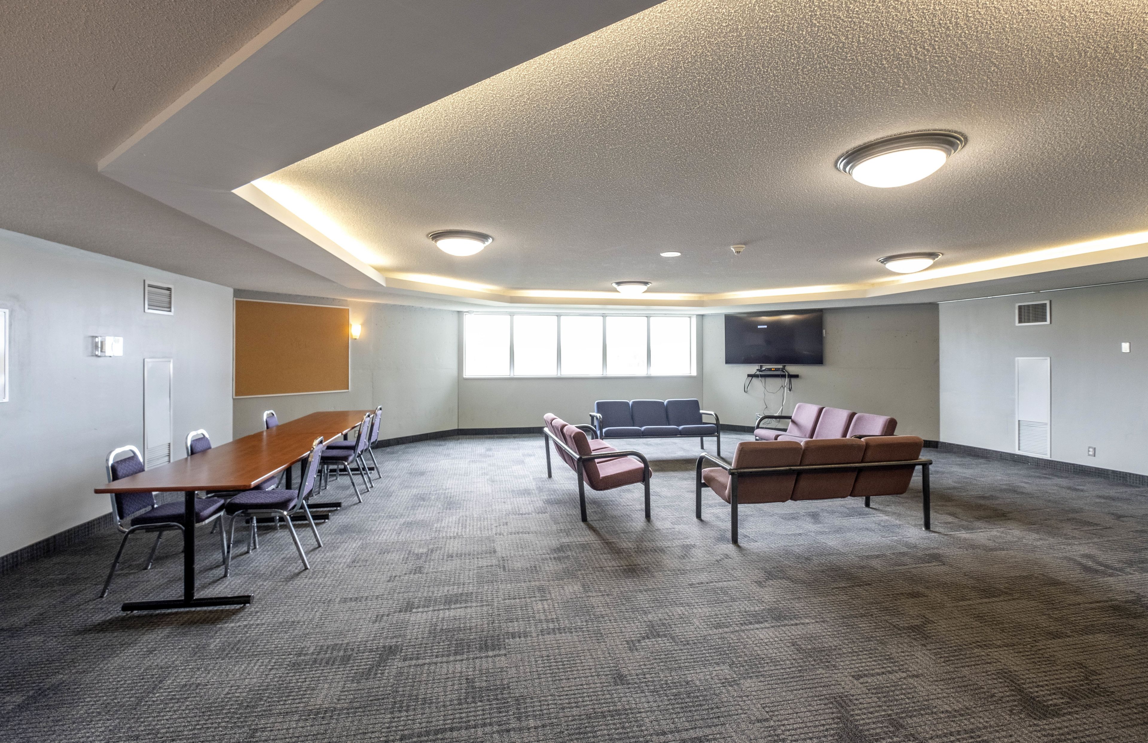 A conference room with a long table, several chairs, a sofa, and a large screen.
