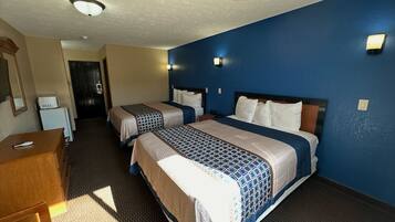 A hotel room with two beds, a desk, and a small kitchenette.
