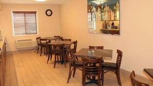 A dining area with a large table and multiple chairs, a clock on the wall, and a window with blinds.