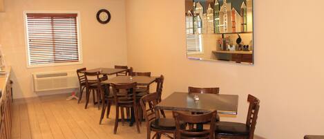 A dining area with a large table and multiple chairs, a clock on the wall, and a window with blinds.