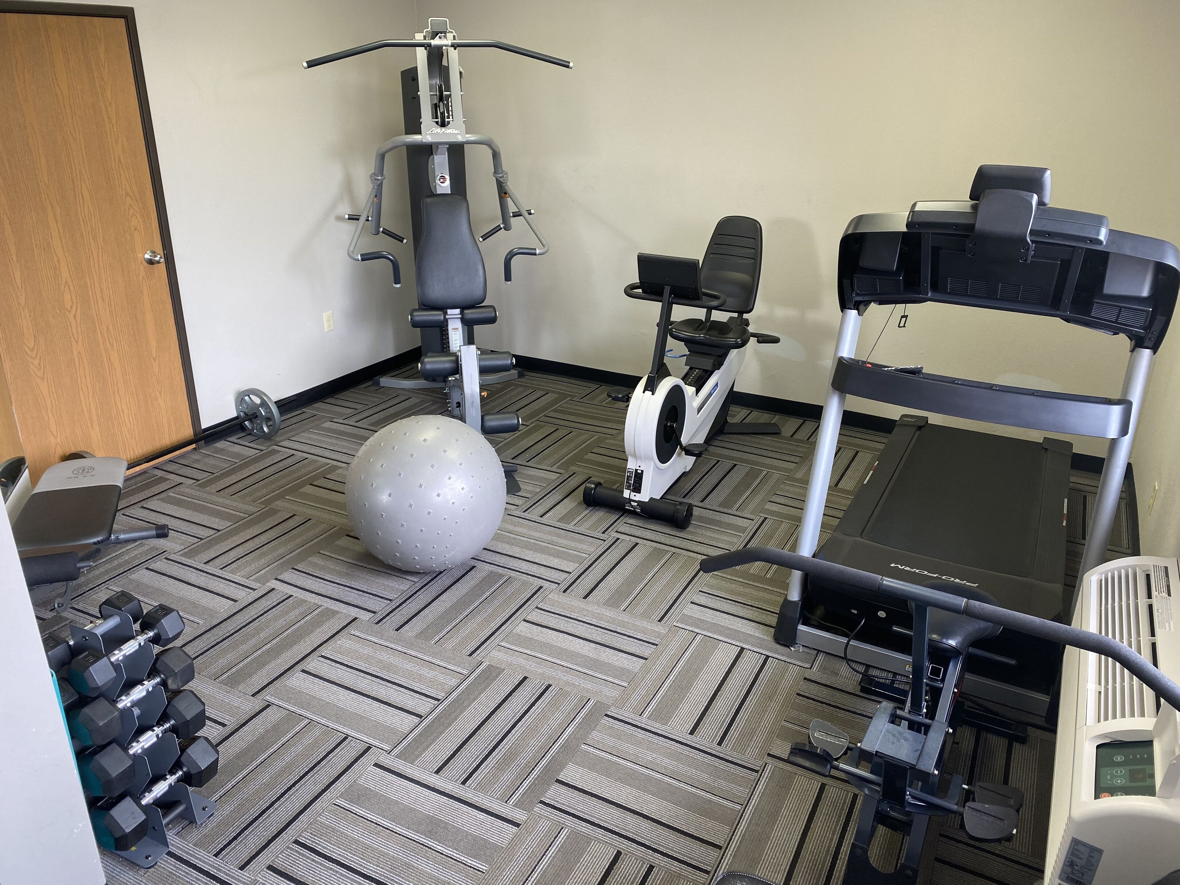 A gym with exercise equipment including a treadmill, elliptical, and free weights.
