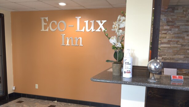 A reception area with a sign reading "Eco-Lux Inn," a vase with white flowers, hand sanitizer, and a mirror. - Eco-Lux Inn (Norfolk)