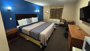 A hotel room with a large bed, a desk, a chair, a television, and a window with curtains.